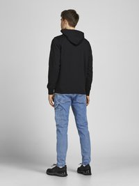 Schwarzer Kapuzenpullover, hellblaue Jeans und schwarze Turnschuhe. Der Hoodie hat einen klassischen Schnitt und ein einfaches Reißverschlussdesign mit einer strukturierten Oberfläche.