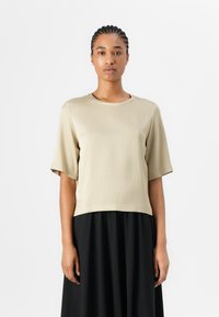 Kortermet, beige, bomullstopp med rund hals, med en avslappet passform og en crop design, parret med en svart, flytende skjørt.