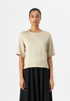 Kortermet, beige, bomullstopp med rund hals, med en avslappet passform og en crop design, parret med en svart, flytende skjørt.