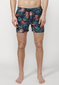 Costume de baie scurt, de culoare bleumarin, cu un model de frunze tropicale în verde și corai. Talie elastică cu șnur, lungime scurtă și material moale.