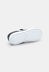 Melnas kedas ar teksturētu auduma augšdaļu, baltu gumijas zoli un zābaku raksta zīmējumu. Velcro siksna aizvēršanai un papildu detaļai.