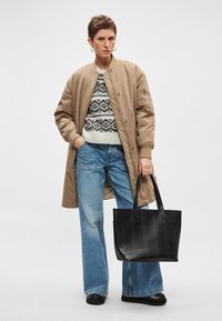 Μπεζ μπουφάν bomber πάνω από ένα λευκό και μαύρο πουλόβερ με σχέδιο, συνδυασμένο με μπλε τζιν παντελόνι με φαρδύ πόδι και μια μαύρη τσάντα tote. Μαύρα επίπεδα παπούτσια.