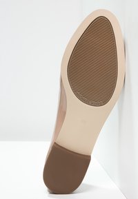 Semelle de chaussure en cuir verni nude avec une texture antidérapante, design plat et branding embossé. La zone du talon est lisse avec une finition beige clair.