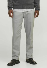 Helle graue Chinos aus glattem Stoff mit geradem Bein. Kombiniert mit schwarzen Lederschuhen und einem dunkelgrauen Pullover.