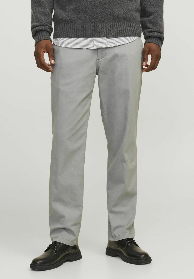 Helle graue Chinos aus glattem Stoff mit geradem Bein. Kombiniert mit schwarzen Lederschuhen und einem dunkelgrauen Pullover.
