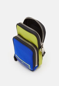 Pochette bicolore Moschino in blu e verde, con zip metallica, patch con logo e tessuto liscio. Forma rettangolare compatta.