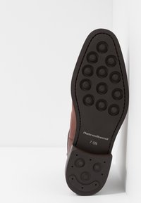 Semelle de chaussure en cuir marron avec un motif de traction circulaire et un matériau en caoutchouc noir. Présente un logo et les détails de taille embossés sur le côté.