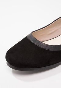 Ballerine plate en daim noir avec un bout arrondi, dotée d'un accent en cuir noir lisse autour de l'ouverture et d'une semelle extérieure texturée pour une meilleure adhérence.