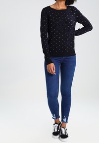 Granatowy sweter dzianinowy w białe groszki, okrągły dekolt, w zestawie z ciemnoniebieskimi obcisłymi dżinsami z postrzępionymi brzegami oraz czarnymi trampkami.