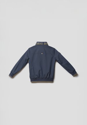 Tumesinine bomberjope elastsest mansetist ja alumisest servast, kollase ja valge triibulise kraega, tagant vaadatuna heledal taustal.