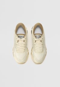 Cream-colored sneakers with a mesh upper, beige accents, rounded toe, and lacing. Features ASICS logo on the tongue and textured sole.