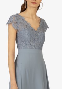Helles blaues Kleid mit einem blumenverzierten Spitzenoberteil, kurzen Ärmeln und einem V-Ausschnitt, kombiniert mit einem glatten, fließenden Rock.