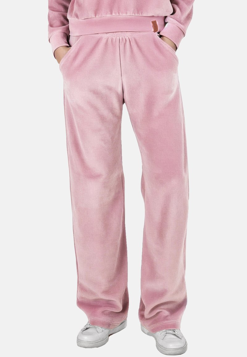 Helle rosa, weite Sweatpants aus Samt mit elastischem Bund und seitlichen Taschen, kombiniert mit weißen Turnschuhen.