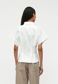 Άσπρο �πουκάμισο κοντό μανίκι με δομημένο σχέδιο, διαθέτοντας αιχμηρό γιακά, πίσω ραφές και εφαρμοστή μέση. Λείο ύφασμα χωρίς ορατά σχέδια.