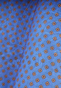 Niebieska tkanina z geometrycznym wzorem małych pomarańczowych kwiatów. Tekstura wydaje się gładka, z delikatnym połyskiem i równomiernie rozmieszczonymi wzorami.