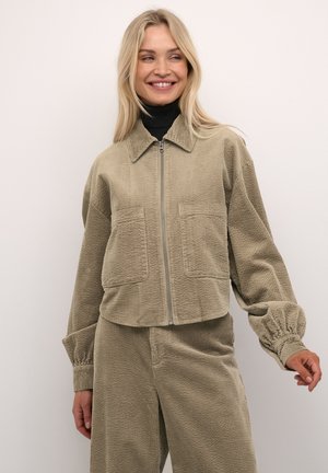 Korte corduroyjas in lichtbeige met een rits aan de voorkant, een kraag en twee voorzakken. Heeft gathered manchetten en een gestructureerde stof.