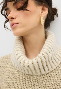 Maglione a girocollo beige in maglia con colletto a coste. Tessuto a trama texture, accentuato con un filo dorato. Grandi orecchini dorati dichiarativi.
