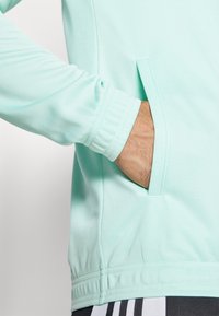 Mintgrüner Sweatshirt mit geripptem Bund, Seitentasche und glatter Textur. Der untere Saum ist ebenfalls vernäht, um erhöhte Haltbarkeit zu gewährleisten.