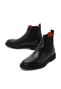 Un paio di stivali Chelsea in pelle nera con pannelli laterali elasticizzati e foderatura interna arancione, presentati su uno sfondo bianco.