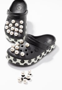 Sabots noirs à gros pois noirs sur semelles blanches, décorés de charms chaussures détachables en perles blanches sur et à côté des chaussures.
