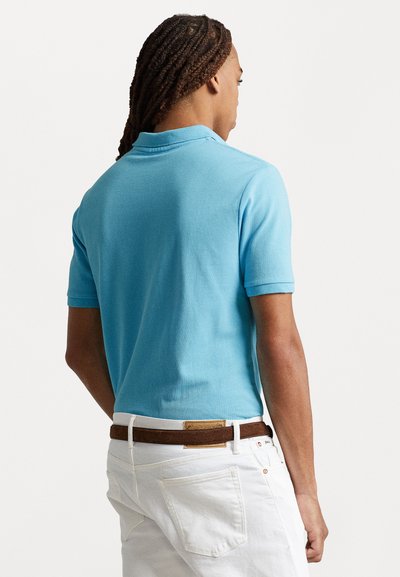 Tricou polo albastru deschis din material texturat, cu maneci scurte si guler clasic. Asortat cu pantaloni albi si o curea maro.