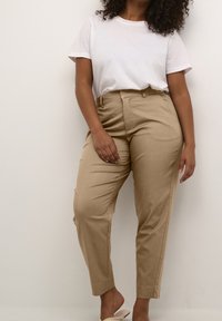 Beige skræddersyede bukser med en glat tekstur, tapered ben, sidelommer og flad front, parret med en ensfarvet hvid kortærmet t-shirt.