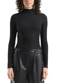 Czarna prążkowana bluzka z długim rękawem i wysokim kołnierzem, zestawiona z czarnymi skórzanymi spodniami z wyraźnymi guzikami i plisowanym przodem.