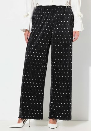 Zwarte, wijde broek met witte stippen, gemaakt van een gestructureerde stof en met een elastische tailleband. De zoom heeft een rafelrand.
