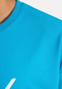 Camiseta de manga corta color turquesa fabricada en algodón suave, con un cuello redondo acanalado y un gran diseño gráfico blanco.
