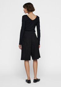 Zwarte langetermijn top met een V-hals en geribbeld textuur, gecombineerd met zwarte knielange shorts met een elastische tailleband en achterzakken.