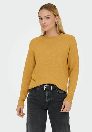 Suéter mostaza de cuello redondo, con mangas raglán largas y un ajuste holgado, combinado con jeans negros de cintura alta y un cinturón negro.