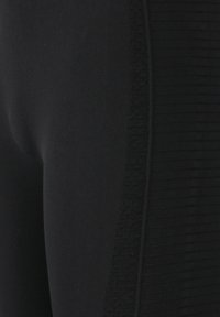 Svarta leggings med slätt tyg och ribbad struktur längs sidorna, som erbjuder en figurnära design och sömlös finish.