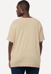 Beige oversized svetr s krátkým rukávem, širokým výstřihem a hladkou texturou, se žebrovaným lemem a bez viditelných vzorů.