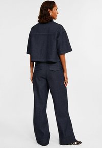 Klippt denimjacka med korta ärmar och mörk randig mönster, i kombination med matchande högmidjade vida byxor.