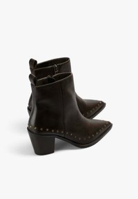 Pareja de botas de cuero marrón oscuro hasta el tobillo con punteras puntiagudas, tacones bajos de bloque, cremalleras laterales y detalles de tachuelas de latón a lo largo de los bordes.