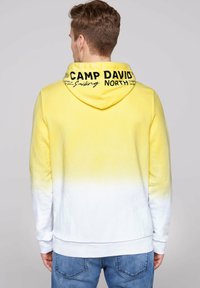 Sudadera con capucha en degradado amarillo y blanco, con cordón, que presenta "CAMP DAVID" y "NORTH" impresos en negro en la parte posterior. Tejido suave, puños acanalados.
