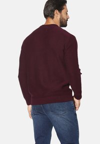 Bordeauxroter Strickpullover mit gerippten Bündchen und Saum, mit strukturierten Seitendetails und lockerem Schnitt, kombiniert mit blauen Jeans aus Denim.