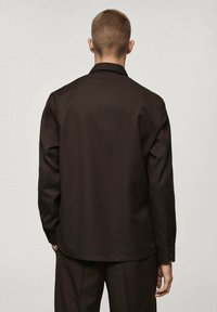 Chemise noire à manches longues avec une coupe droite, un empiècement au dos et des poignets à boutons, fabriquée en tissu lisse. Design minimaliste et couleur unie.
