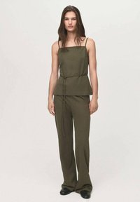 Olijfgroen, mouwloos top met een vierkant decolleté en een riem in de taille, gecombineerd met wijde broekspijpen van dezelfde stof en kleur.
