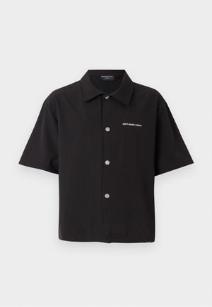 Camisa preta de manga curta em tecido leve, com design abotoado, botões prateados e texto bordado: "não desperdice a cultura."