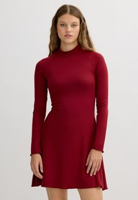 Vestido rojo de manga larga con cuello alto, hecho de un material suave y ajustado. La falda se ensancha suavemente en el dobladillo, creando una sutil forma de A.