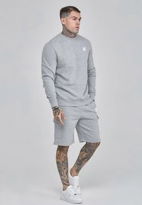 Sivá mikina s okrúhlym výstrihom a rebrovanými manžetami, doplnená sivými šortkami s bočnými vreckami. Biele tenisky dotvárajú ležérny vzhľad.