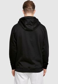 Svart hoodie med mjuk textur, med en kenguruficka och ribbade muddar, visad bakifrån mot en neutral bakgrund.