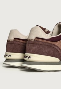 Sneakers marroni e beige con una tomaia in suede e pelle, dettagli testurizzati, una suola spessa con ammortizzazione e strisce bianche e grigie a contrasto.