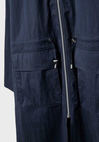 Giacca blu navy con cerniera frontale, due grandi tasche con patta e coulisse regolabili con fermagli in metallo in vita.