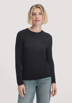 Schwarzes Langarmshirt in figurbetonter Passform, aus glattem Stoff gefertigt, mit einem runden Halsausschnitt und zartem Glanz, kombiniert mit hellblauen Jeans.