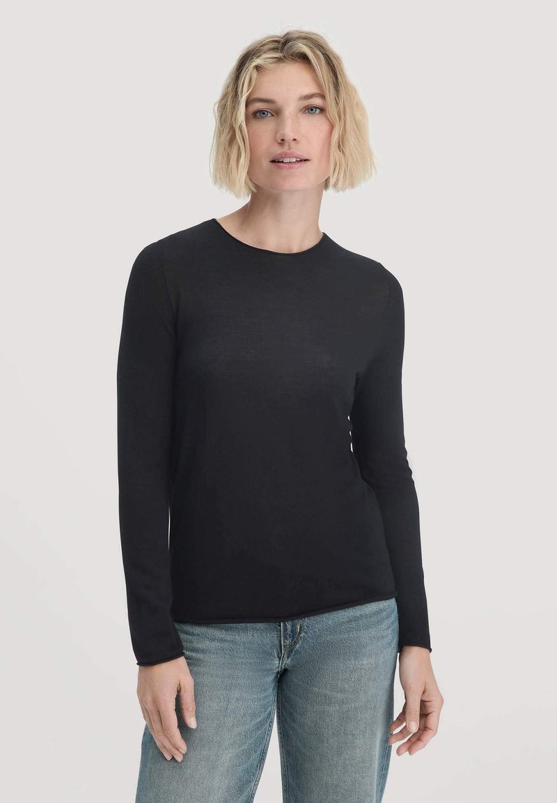 Schwarzes Langarmshirt in figurbetonter Passform, aus glattem Stoff gefertigt, mit einem runden Halsausschnitt und zartem Glanz, kombiniert mit hellblauen Jeans.