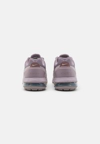 Violetti verkkokudoksiset lenkkarit harmailla yksityiskohdilla, joissa on näkyvä ilmatyynypohja, pyöreä muoto ja teksturoidut kuviot yläosassa.