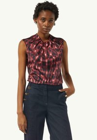 Bluzka z krótkim rękawem w bogatym burgundowym kolorze o jedwabistej fakturze i abstrakcyjnym czarnym wzorze. W komplecie z granatowymi spodniami z akcentami w postaci złotych guzików.