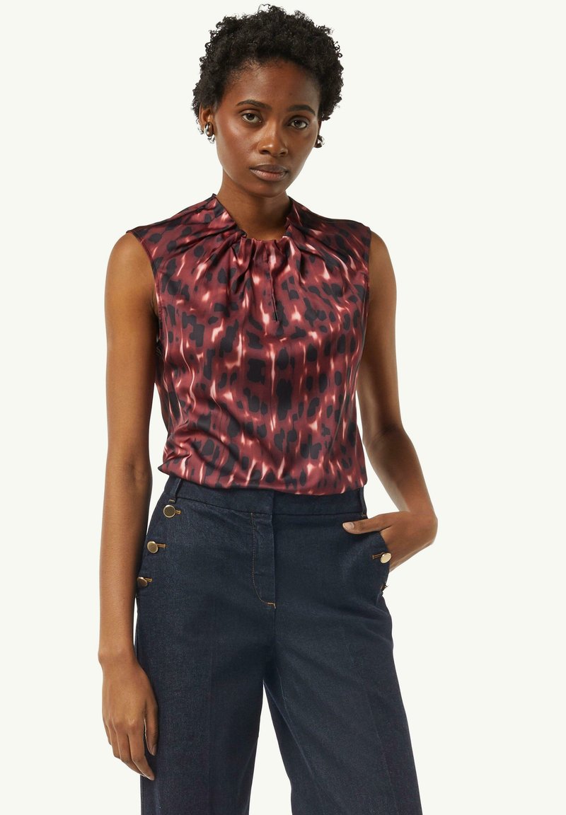 Bluzka z krótkim rękawem w bogatym burgundowym kolorze o jedwabistej fakturze i abstrakcyjnym czarnym wzorze. W komplecie z granatowymi spodniami z akcentami w postaci złotych guzików.